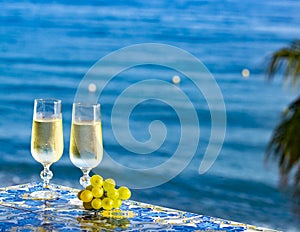 Romantic event, bottle with cold sparkling wine, cava or champagne served with two glasses on table with sea view and palm tree