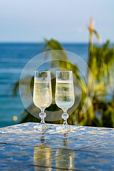 Romantic event, bottle with cold sparkling wine, cava or champagne served with two glasses on table with sea view and palm tree