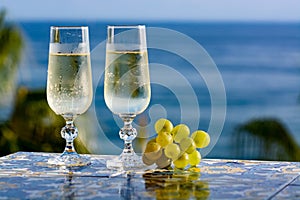 Romantic event, bottle with cold sparkling wine, cava or champagne served with two glasses on table with sea view and palm tree