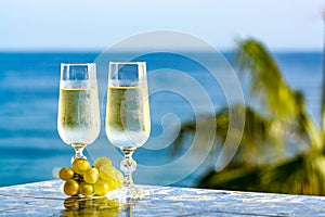 Romantic event, bottle with cold sparkling wine, cava or champagne served with two glasses on table with sea view and palm tree