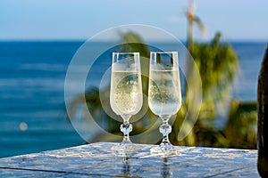 Romantic event, bottle with cold sparkling wine, cava or champagne served with two glasses on table with sea view and palm tree