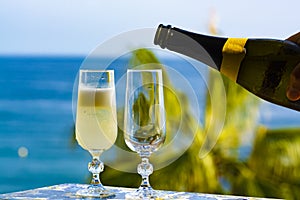 Romantic event, waiter pouring cold sparkling wine, cava or champagne served with two glasses on table with sea view and palm tree