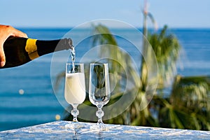 Romantic event, waiter pouring cold sparkling wine, cava or champagne served with two glasses on table with sea view and palm tree