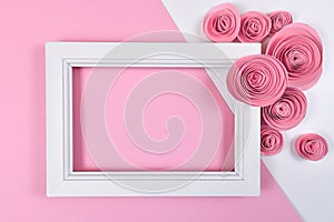 Romantic flat lay with empty white picture frame surrounded by paper craft roses on pink background