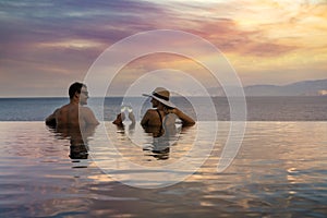 Romantic getaways - couple drinking champagne and enjoying beautiful sunset in pool at tropical resort