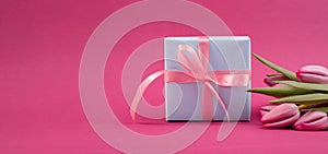 Romantic gift box tied with big pink bow and spring tulips on pink color background. Mother& x27;s day or Easter holiday