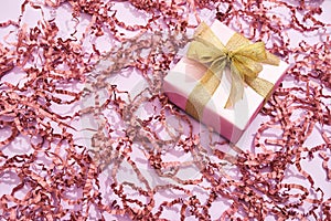 Romantic gift for Womens Day. Top view of a small wrapped gift box with golden bow on pink background with decorative