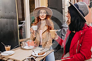 Romantic ginger girl have lunch with best friend in warm autumn weekend. Portrait if two ladies in hats talking in