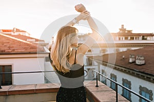 Romantic girl with blonde hair spending time outdoor enjoying sunrise in summer morning. Portrait from back of elegant