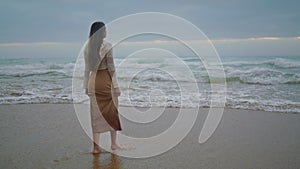 Romantic girl looking ocean view evening. Dreamy woman walking on stormy beach