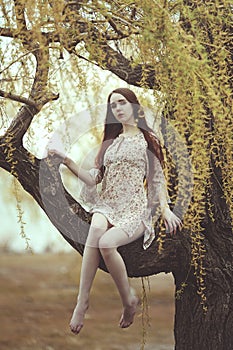 Romantic girl with red long hair in the wind on the willow tree.