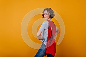 Romantic girl with serious face expression posing in red supehero cloak. Indoor photo of confident female model with