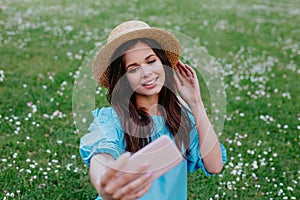 Romantic girl sitting on a green lawn with a smartphone in hand and takes selfie