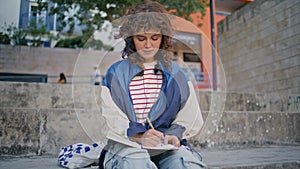 Romantic girl writing notebook at neighborhood. Curly relaxed woman making notes