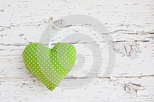 Romantic green dotted heart shape hanging above white wooden surface on a nail- white wooden shabby chic background for