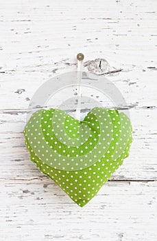 Romantic green dotted heart shape hanging above white wooden surface on a nail- white wooden shabby chic background for