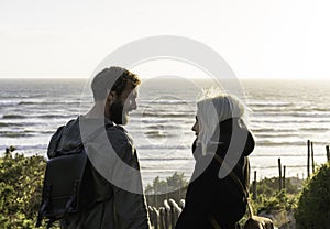 Romantic happy couple in love standing on wooden stairs on dunes at the wild beach in front of the sea - Boyfriend and girlfriend