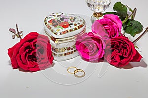 Romantic heart shaped artistic jewelry box with bright red and pink roses with gold engagement rings on light background.