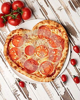 Romantic heart shaped pizza with tomato slices on white wooden table background. Top view. Valentine day concept