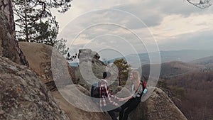 Romantic hikers sitting on the top of the mountain, chatting, and enjoying their time together. A boy with a fancy