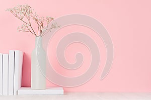 Romantic home decor of white dry flowers in vase and pile white books on light pink background.