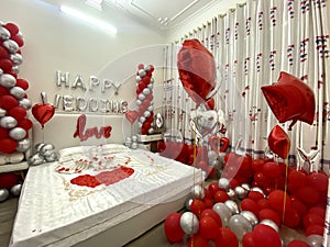 Romantic honeymoon bedroom decoration with a couple of swans kissing made from towels, balloons, and rose petals