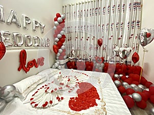 Romantic honeymoon bedroom decoration with a couple of swans kissing made from towels, balloons, and rose petals