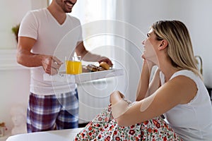 Romantic husband waking wife with breakfast in bed