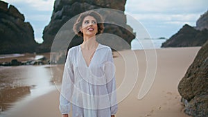 Romantic lady admiring beach on rocky island. Smiling woman walking sandy coast