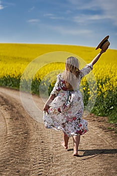 Romantic latino woman barefoot on a road in canola field