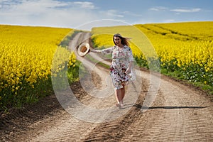 Romantic latino woman barefoot on a road in canola field