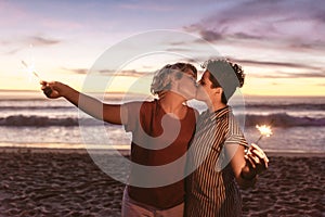 Romantic lesbian couple kissing and holding sparklers at the beach