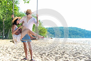 Romantic lifestyle asian couple lover playing an ukulele on the hammock. relax and honeymoon in luxury resort near the beach.