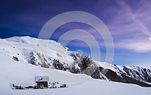 Romantic log cabin on top of snowy mountain photographed at night