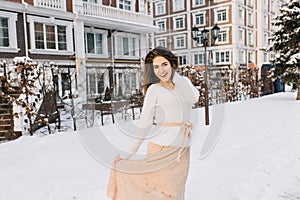 Romantic long-haired girl in skirt posing on the street full of snow with lantern on background. Outdoor portrait of