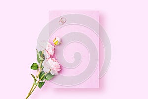 A romantic love letter that is yet to be written with wedding rings and rose on pink background. Flat lay image