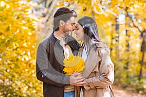 Romantic lovers with bunch of golden leaves cuddling at forest