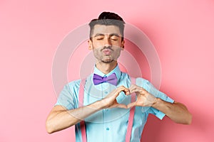 Romantic man in funny bow-tie waiting for kiss, close eyes and pucker lips kissing, showing heart gesture, being in love