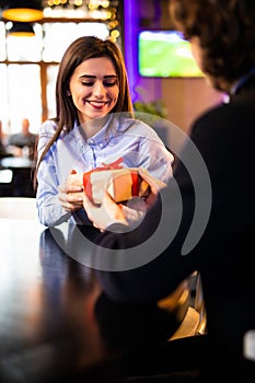 Romantic man giving birthday gift to beautiful emotional woman. Portrait of lovely couple sitting together in cafe, dating.