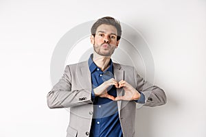 Romantic man in suit showing heart sign and pucker lips for kiss, express love and passion, like his lover, standing on