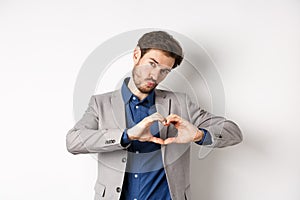 Romantic man in suit showing heart sign and pucker lips for kiss, express love and passion, like someone, standing on