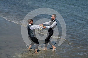 Romantic men same sex marriage. Gay grooms walking together on sea beach during Wedding day. Romantic men in sea water.