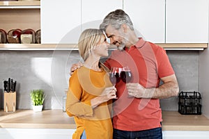 Romantic middle aged couple drinking red wine at kitchen, cuddling