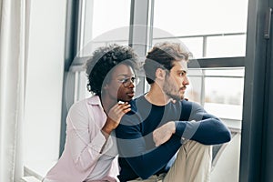 Romantic mixed race couple standing by the window thinking about their future.