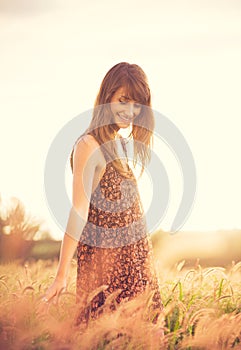 Romantic Model in Sun Dress in Golden Field at Sunset