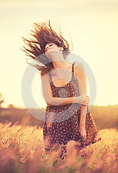 Romantic Model in Sun Dress in Golden Field at Sunset