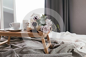 Coffee table on bed. Flowers, coffee cup and candles. Interior gray tones, plaid