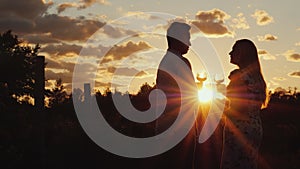 Romantic multi-ethnic couple drinking wine at sunset. They stand near the vineyard. Honeymoon and travel concept