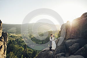 Romantic newlywed couple posing in sunset lights on majestic roc