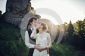 Romantic newlywed couple posing in sunset lights on majestic roc